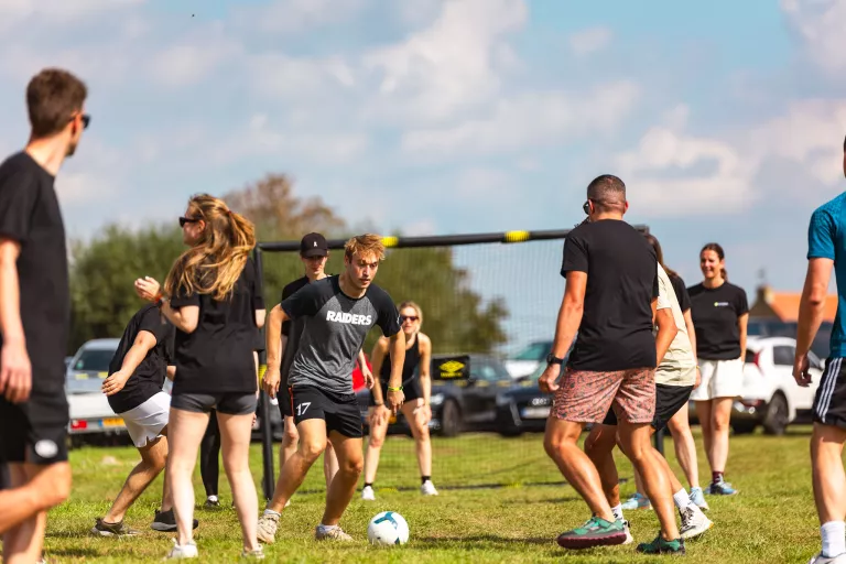 A group of Springbok Agency people playing soccer on a sunny grassy field. The mood is energetic and lively as one player focuses on a ball. Cars are in the background.