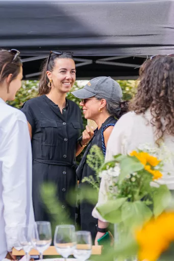 Three smiling women chat at Springbok's barbecue event under a canopy. It's sunny, with sunflowers in the foreground.