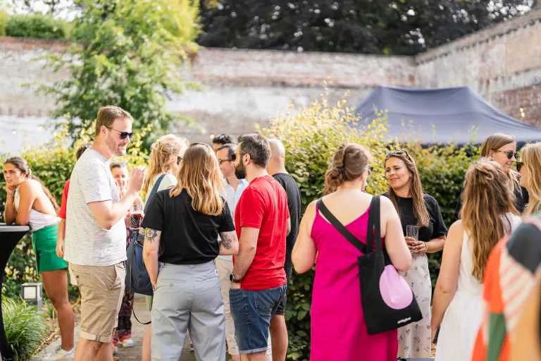 A group of people socializing at a Springbok summer barbecue event, surrounded by greenery and a brick wall. They're smiling and casually dressed, suggesting a relaxed atmosphere.