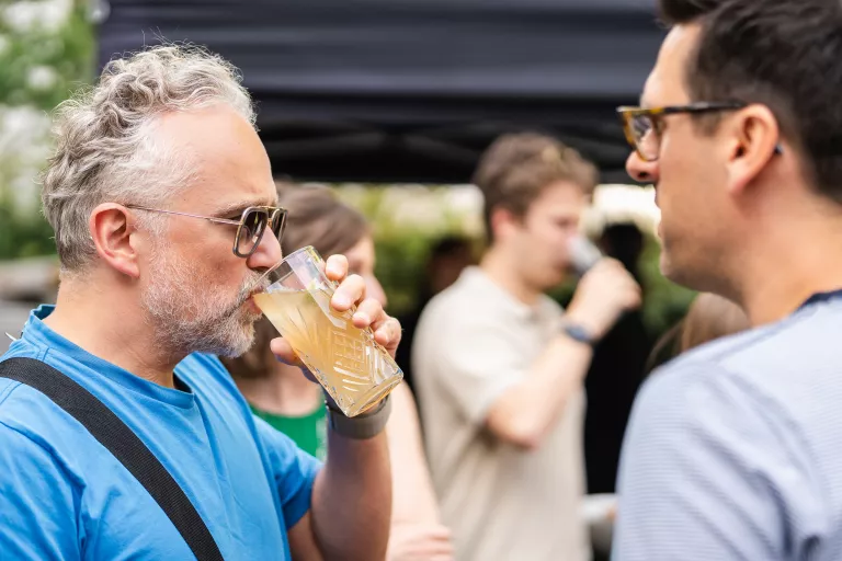 Close-up of two men with glasses enjoying a chat and drink at Springbok's outdoor summer barbecue in Ghent. 