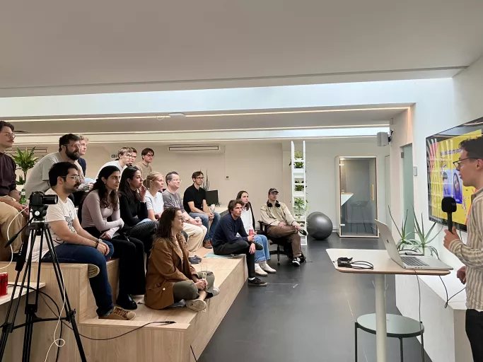 A presenter speaks to an engaged audience in the modern, bright Springbok office space in Mechelen, featuring a large screen and greenery.